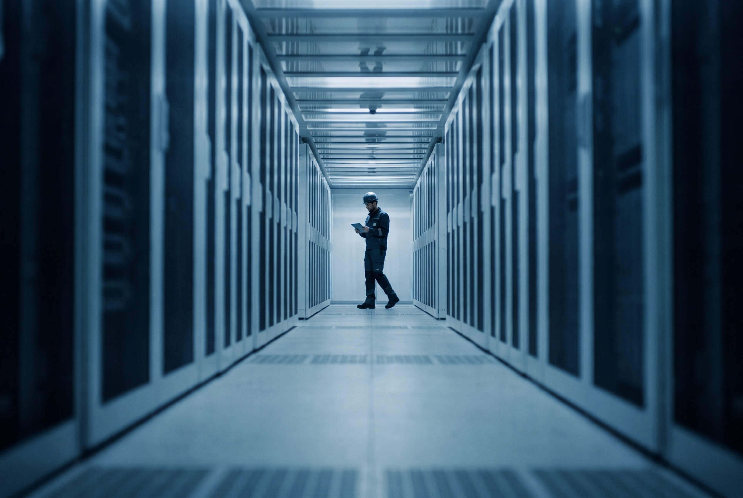 An engineer with a tablet at the end of a long aisle of server racks